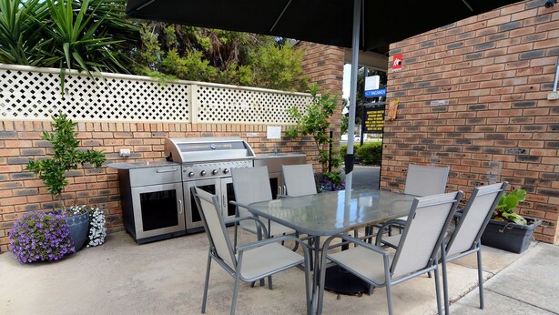 Un patio exterior con una parrilla, mesa y sillas.