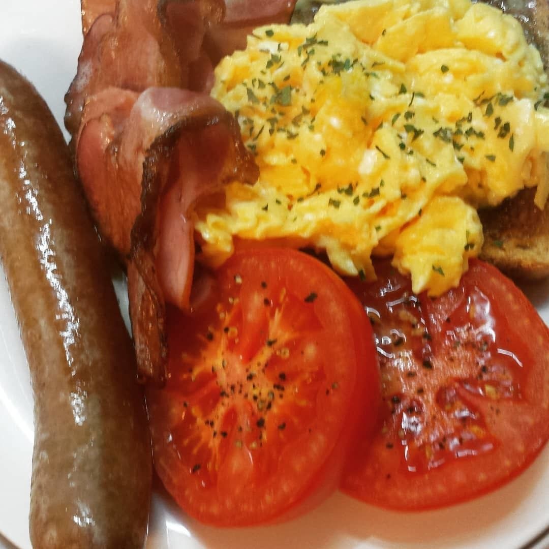 A plate with scrambled eggs, bacon, sausages, and tomato slices.