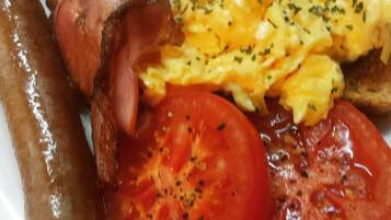 A plate with scrambled eggs, bacon, sausages, and tomato slices.