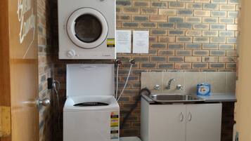 A compact laundry area with a front-loading washing machine and a wall-mounted dryer. There is a sink with a faucet and a soap dispenser on the counter.