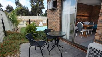 A patio with two black wicker chairs and a round table, a brick wall, and a sliding glass door leading to an indoor area with a table and chairs.