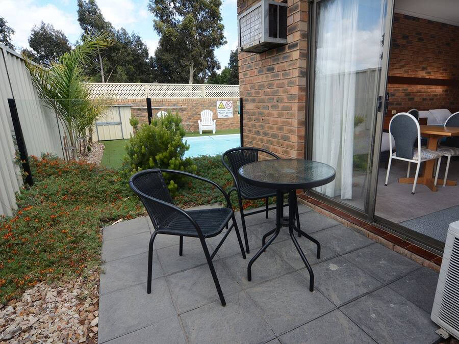 A patio with two black wicker chairs and a round table, a brick wall, and a sliding glass door leading to an indoor area with a table and chairs.