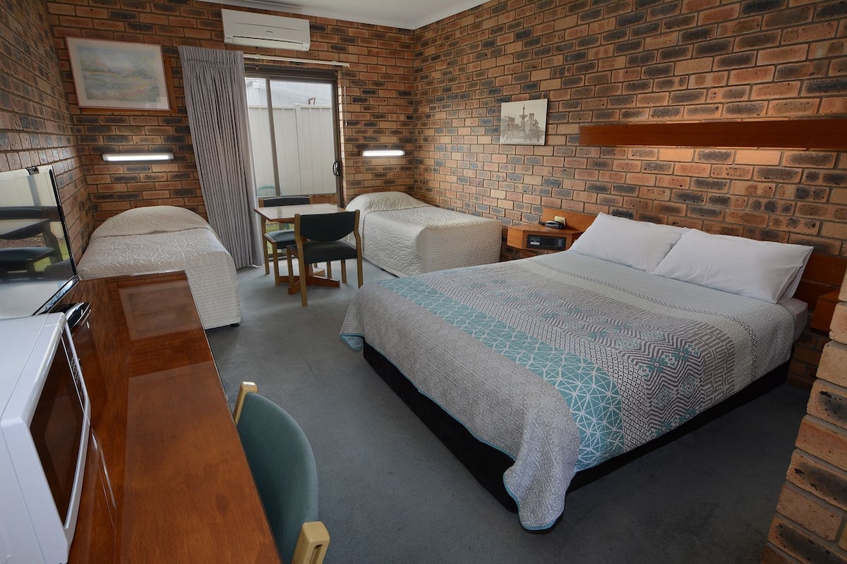 Habitación de hotel con pared de ladrillo, cama con ropa de cama estampada, escritorio con silla y una mesita pequeña.