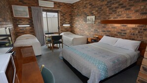 Habitación de hotel con pared de ladrillo, cama con ropa de cama estampada, escritorio con silla y una mesita pequeña.