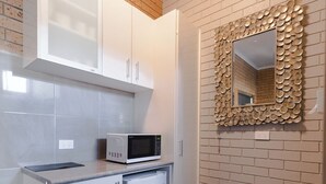 Una cocina con armarios blancos, un microondas y un espejo decorativo sobre una pared de ladrillo.
