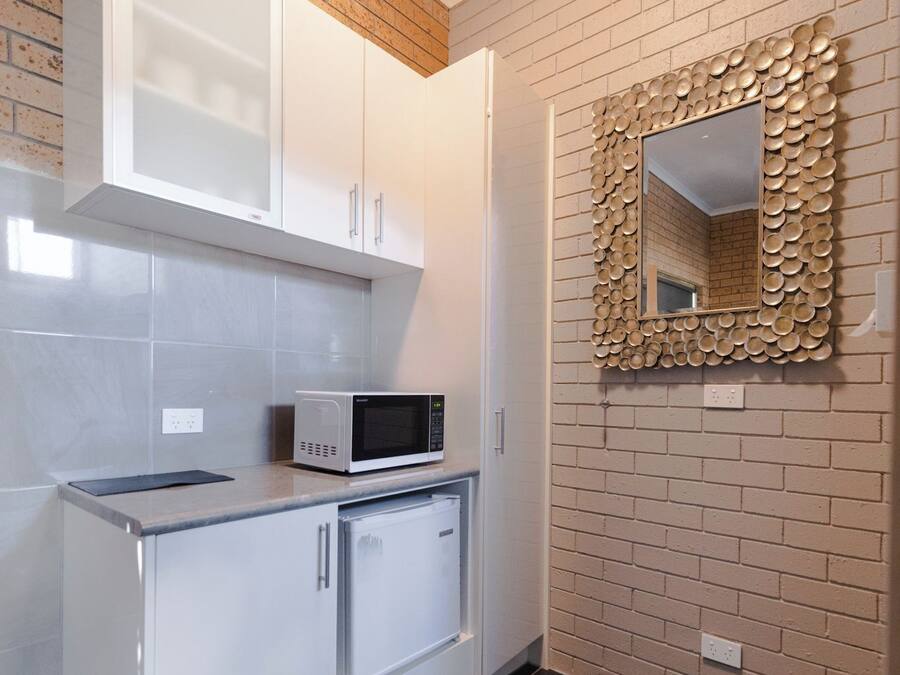A kitchen with white cabinets, a microwave, and a decorative mirror on a brick wall.