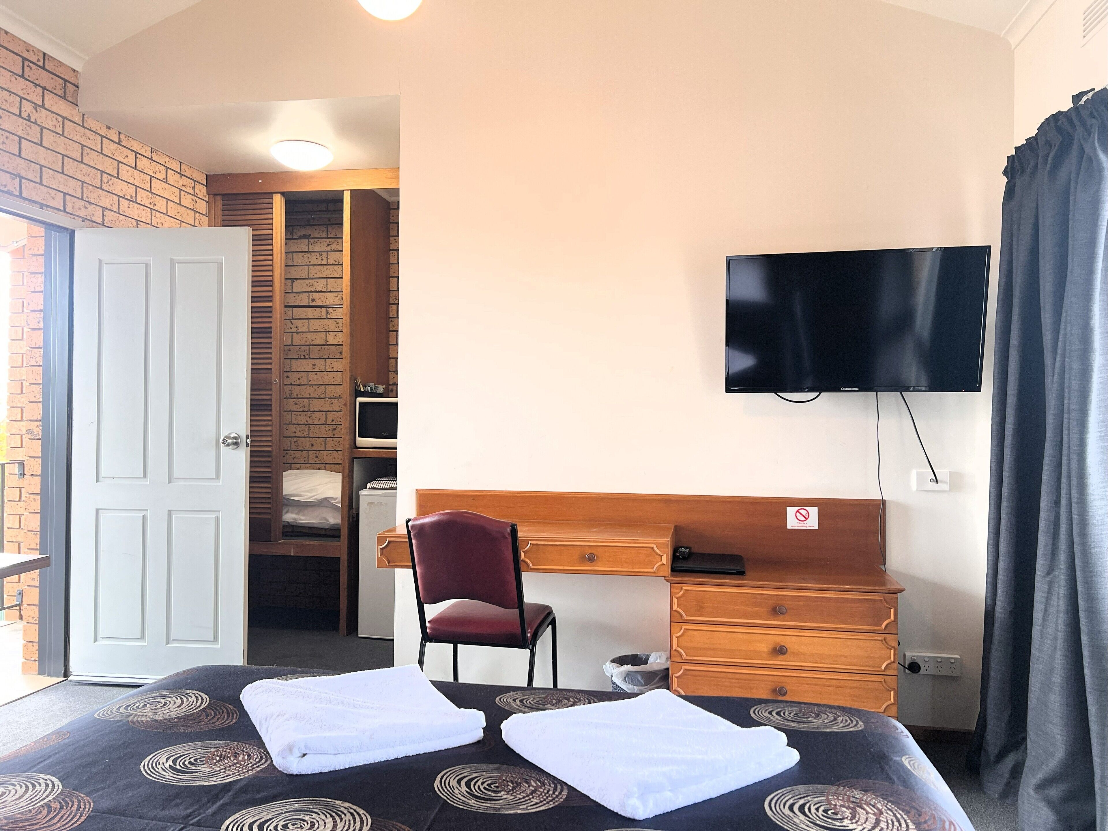 A hotel room with a bed, a desk, a chair, a television, and a bathroom visible through an open door.