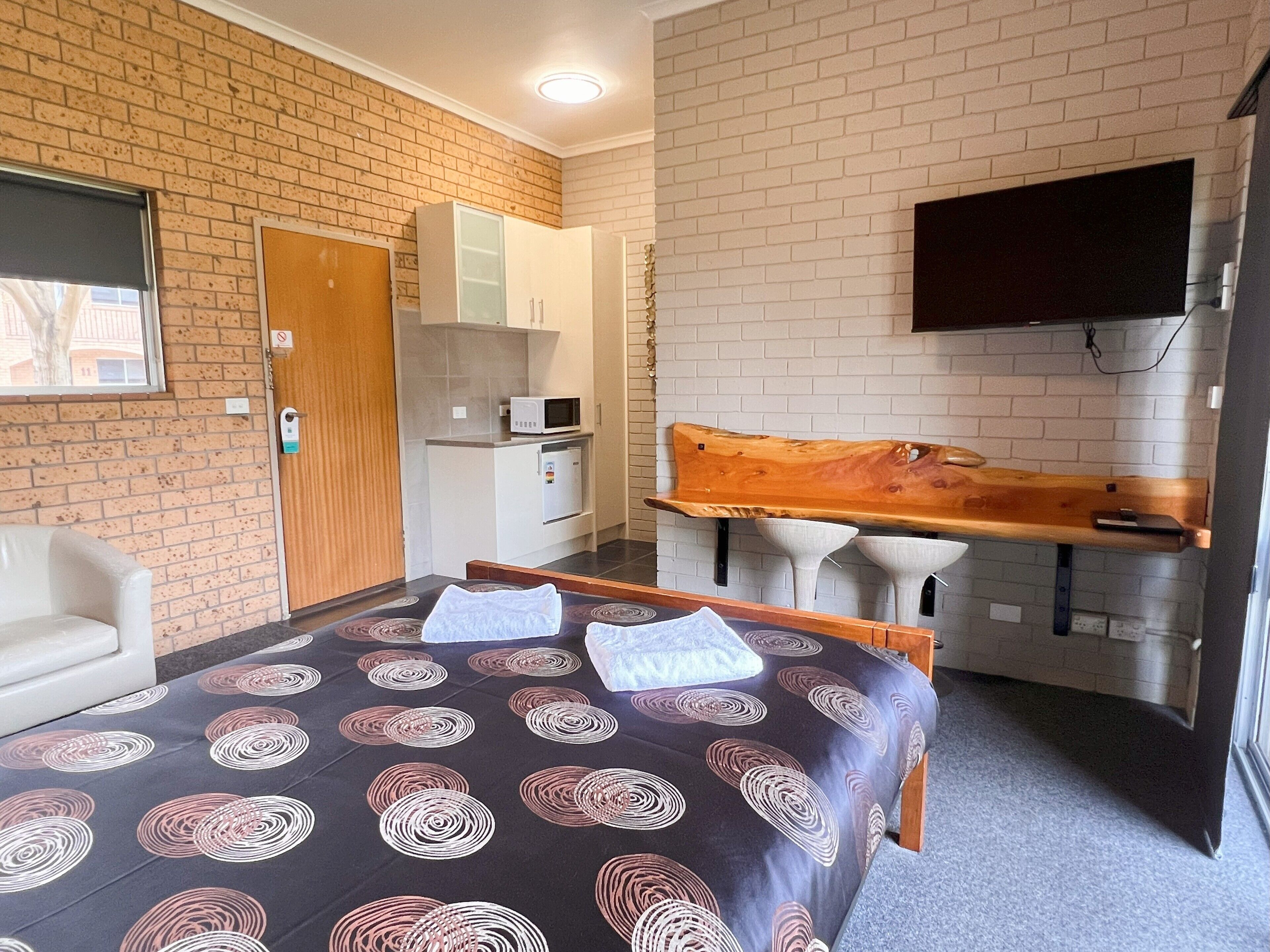 A hotel room with a bed, a desk with a chair, a TV mounted on the wall, and a microwave.