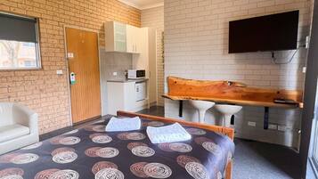 A hotel room with a bed, a desk with a chair, a TV mounted on the wall, and a microwave.