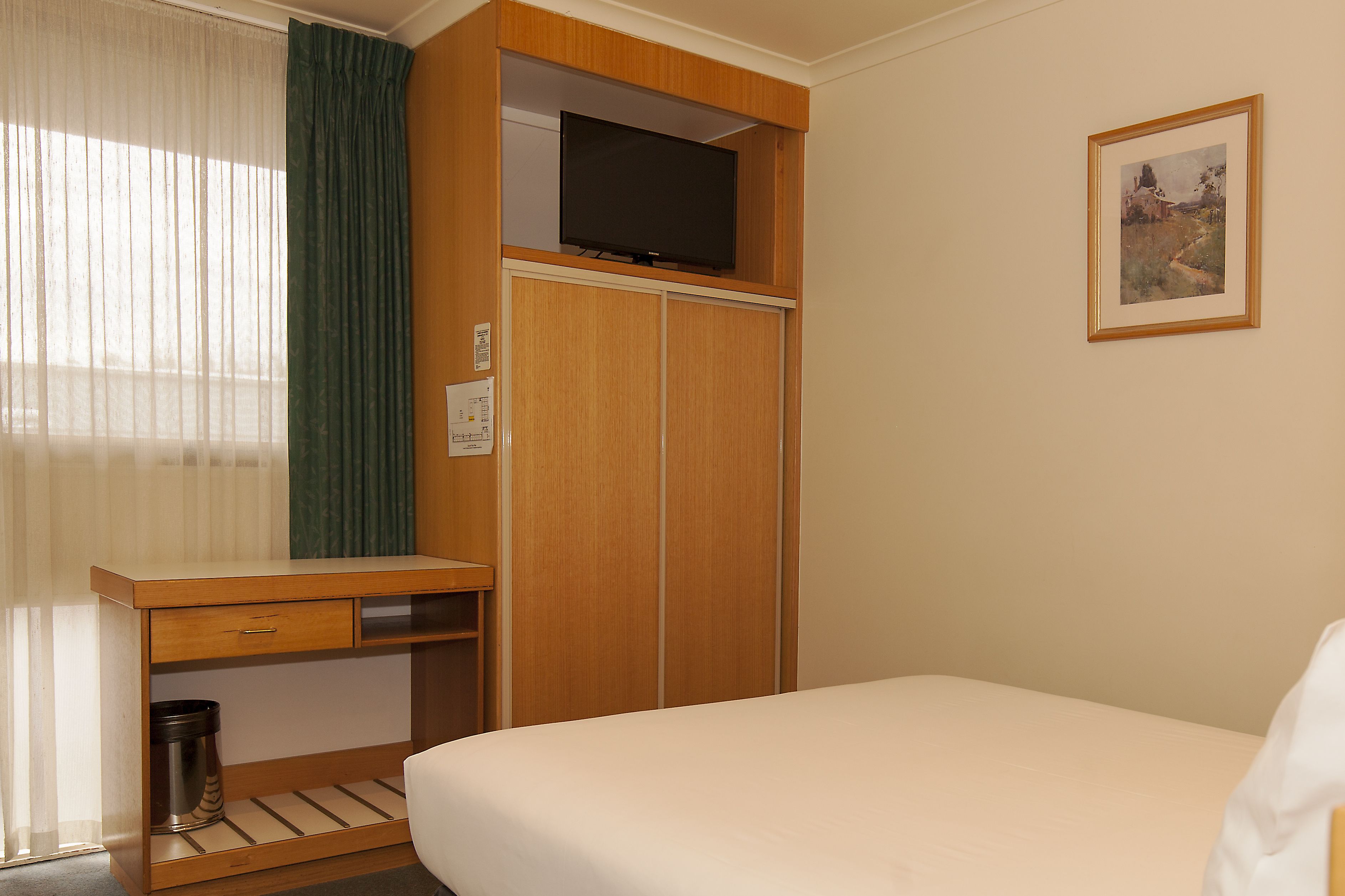 Une chambre d’hôtel avec un lit, un bureau avec une télévision et un tableau encadré au mur.