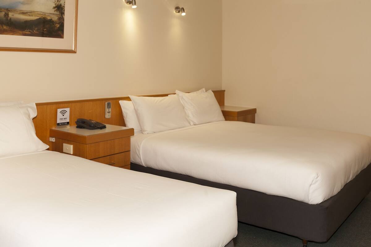 Quarto de hotel com duas camas de solteiro, cabeceiras de madeira, mesas de cabeceira, um quadro pendurado na parede e um símbolo de Wi-Fi.