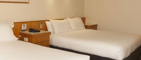 Habitación de hotel con dos camas individuales, cabeceros de madera, mesitas de noche, un cuadro en la pared y el símbolo de Wi-Fi.
