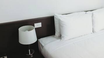 A neatly made bed with white bedding and pillows, a white bedside lamp, and a dark-colored nightstand.