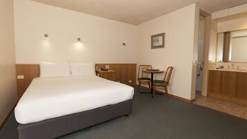 A hotel room with a large bed, a small table with chairs, a desk, and a bathroom with a mirror and sink.