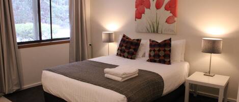 A neatly made bed with a gray and white bedspread, two side tables with lamps, and a painting of red flowers on the wall.