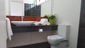 A modern bathroom with a large sink, a toilet, and a mirror above the sink. There are towels and toiletries on the sink counter.