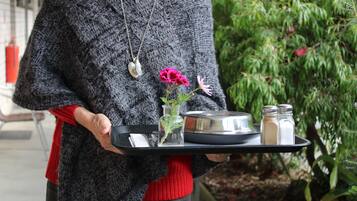 Une personne tenant un plateau sur lequel se trouvent un pot, un vase avec des fleurs, ainsi que des salières et des poivrières.