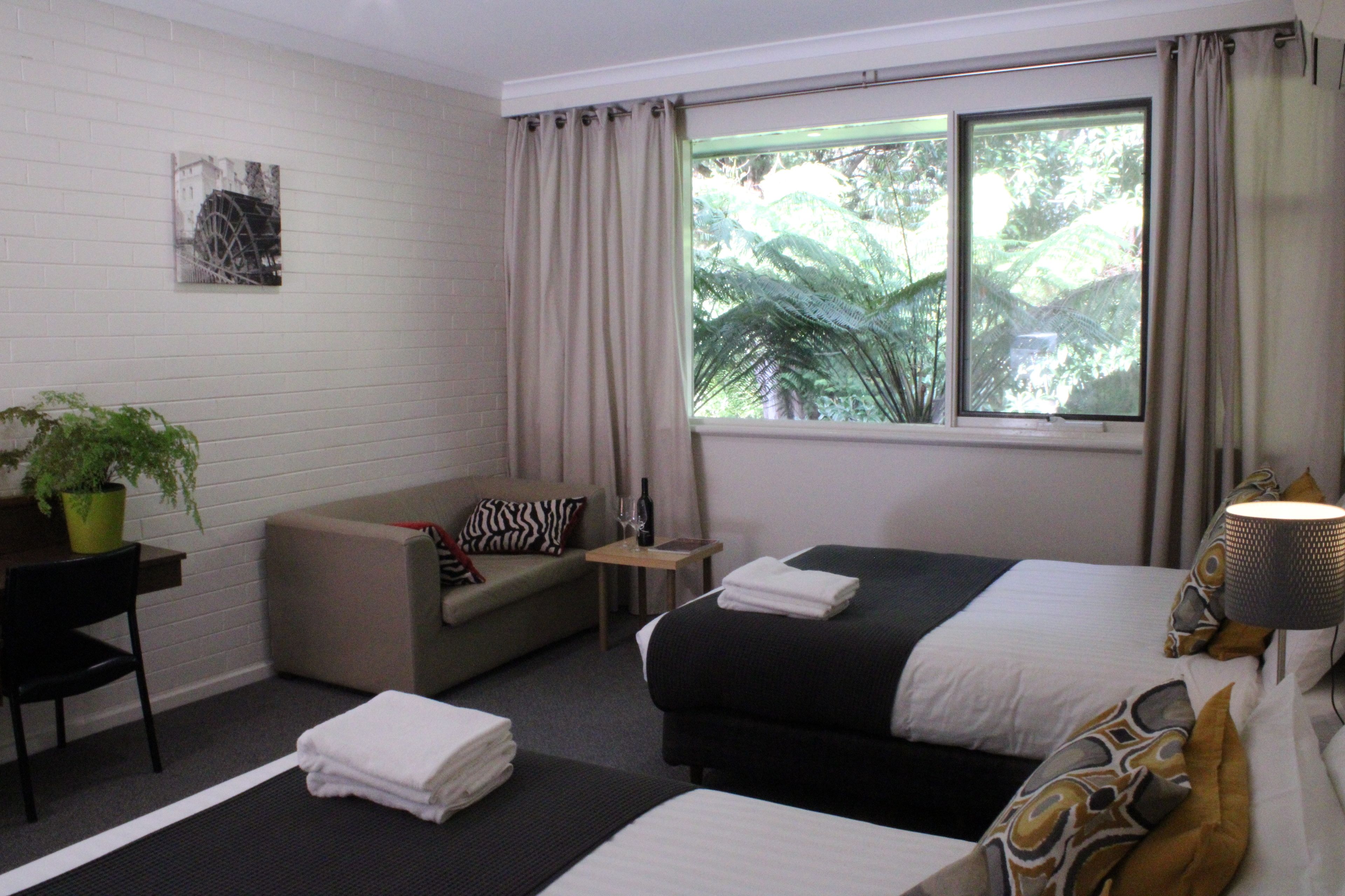 A hotel room with a bed, a sofa, a desk, a potted plant, and a window with curtains.