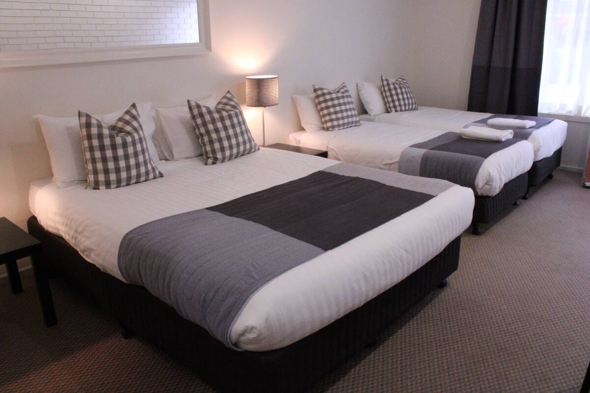 A hotel room with two beds, each with a checkered pillow, a bedside lamp, and a window with curtains.