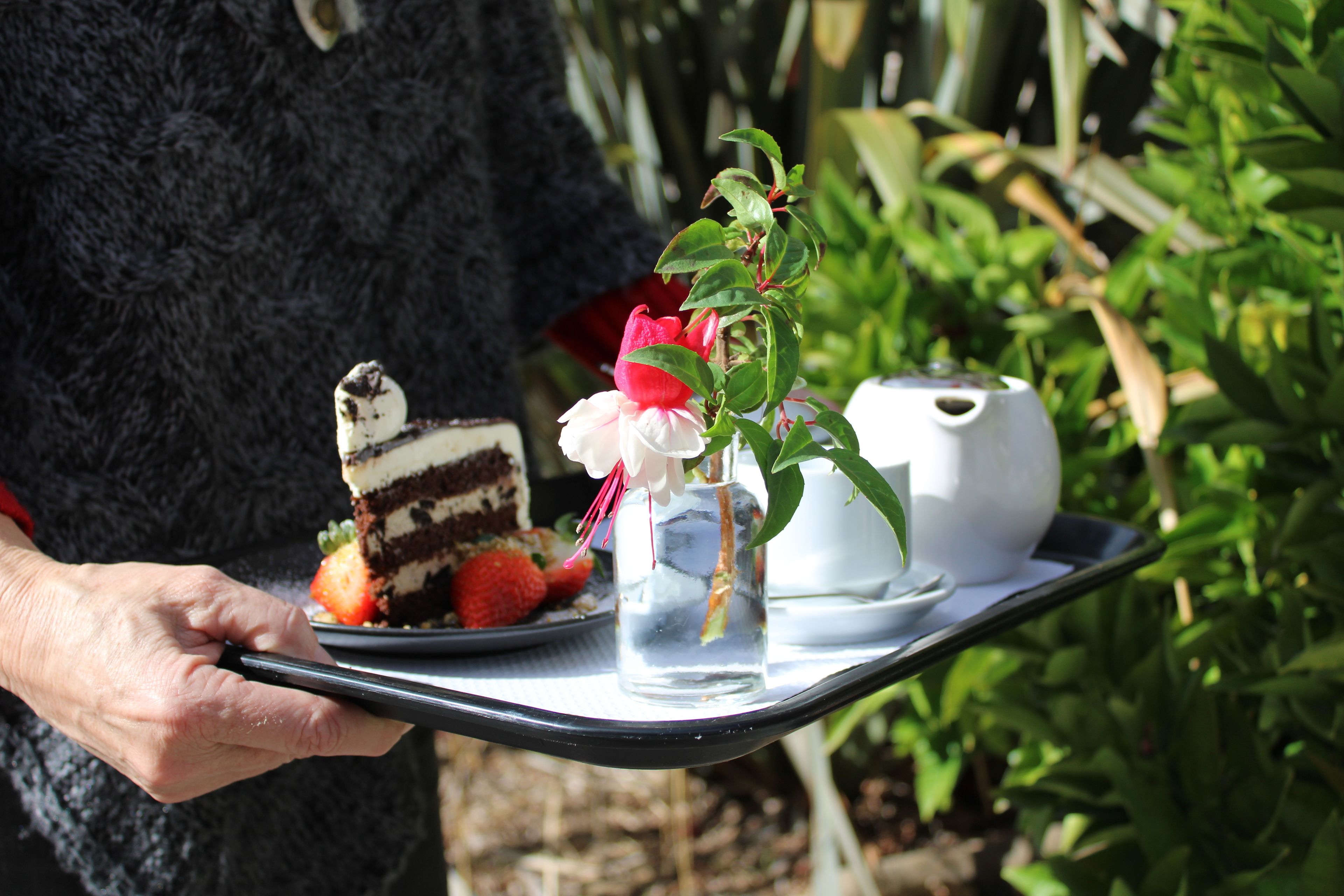 A tray with a slice of cake, strawberries, a white teapot, and a small vase with a flower.