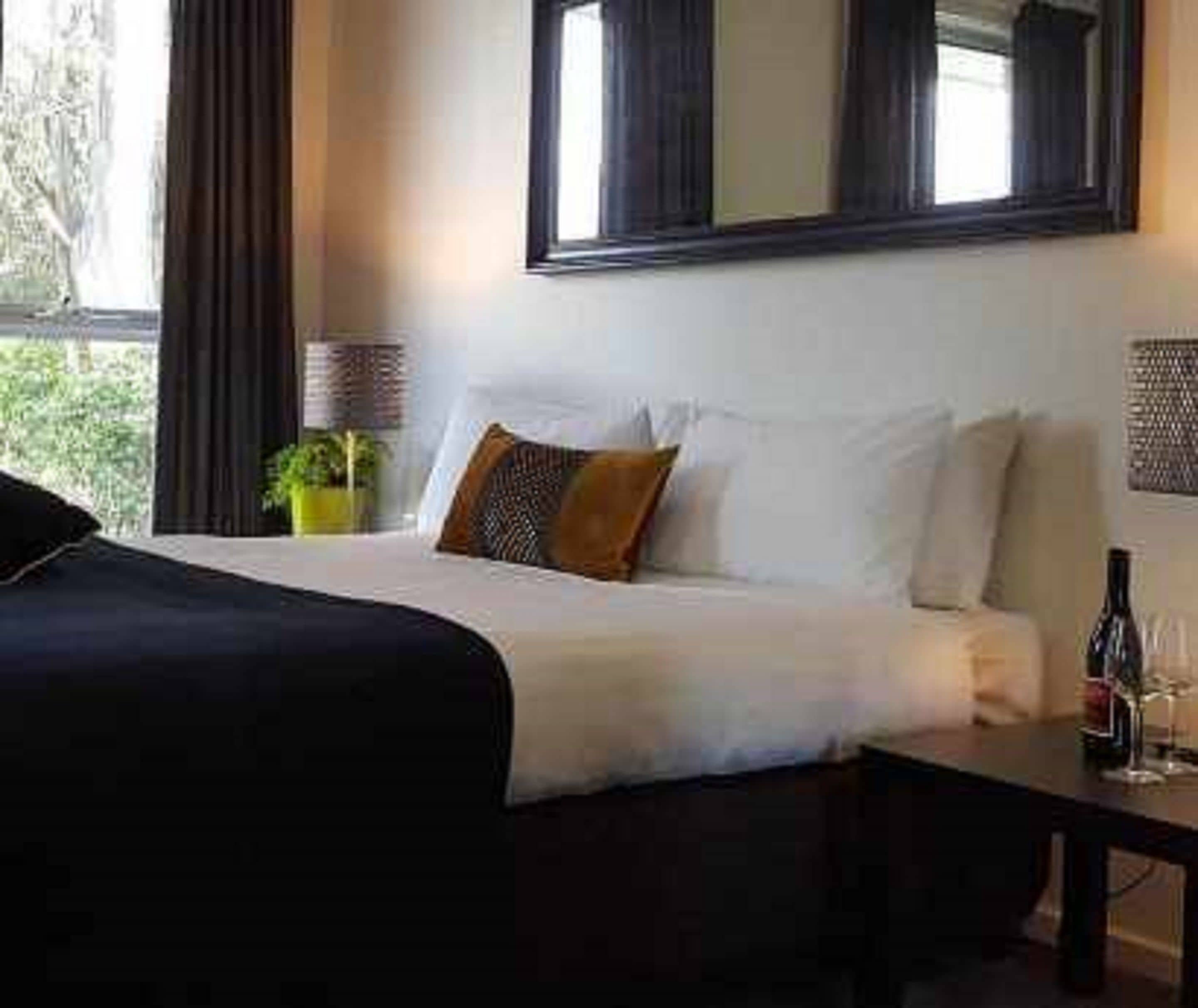 Una habitación de hotel con una cama, una mesita de noche, una lámpara y un ventanal con cortinas.