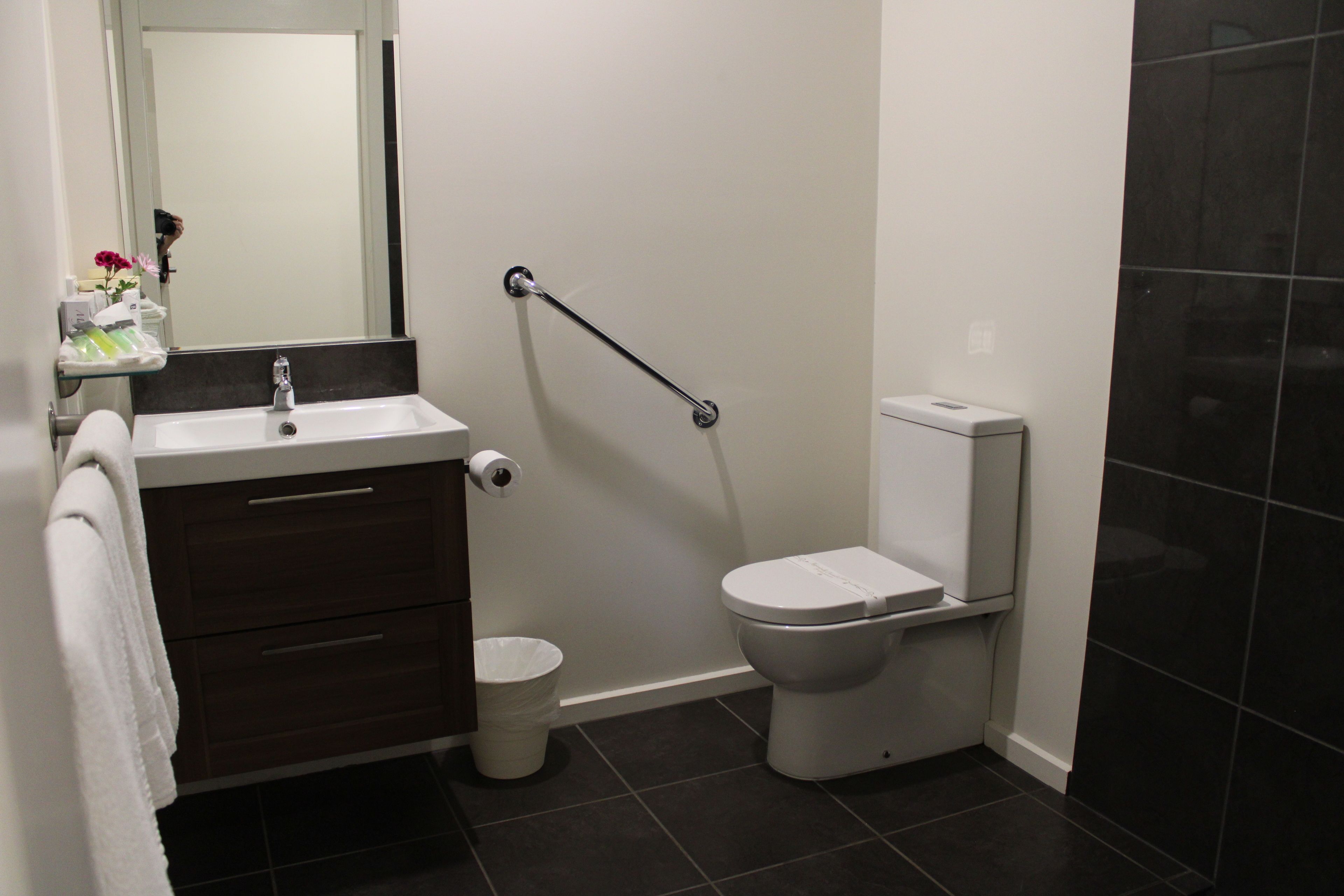 A modern bathroom with a white sink, dark brown vanity, a white toilet, and a grab bar.