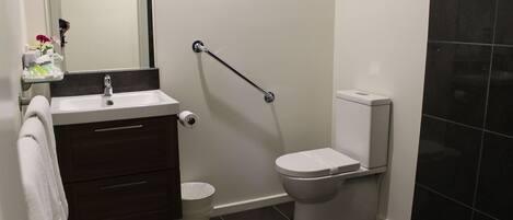 A modern bathroom with a white sink, dark brown vanity, a white toilet, and a grab bar.