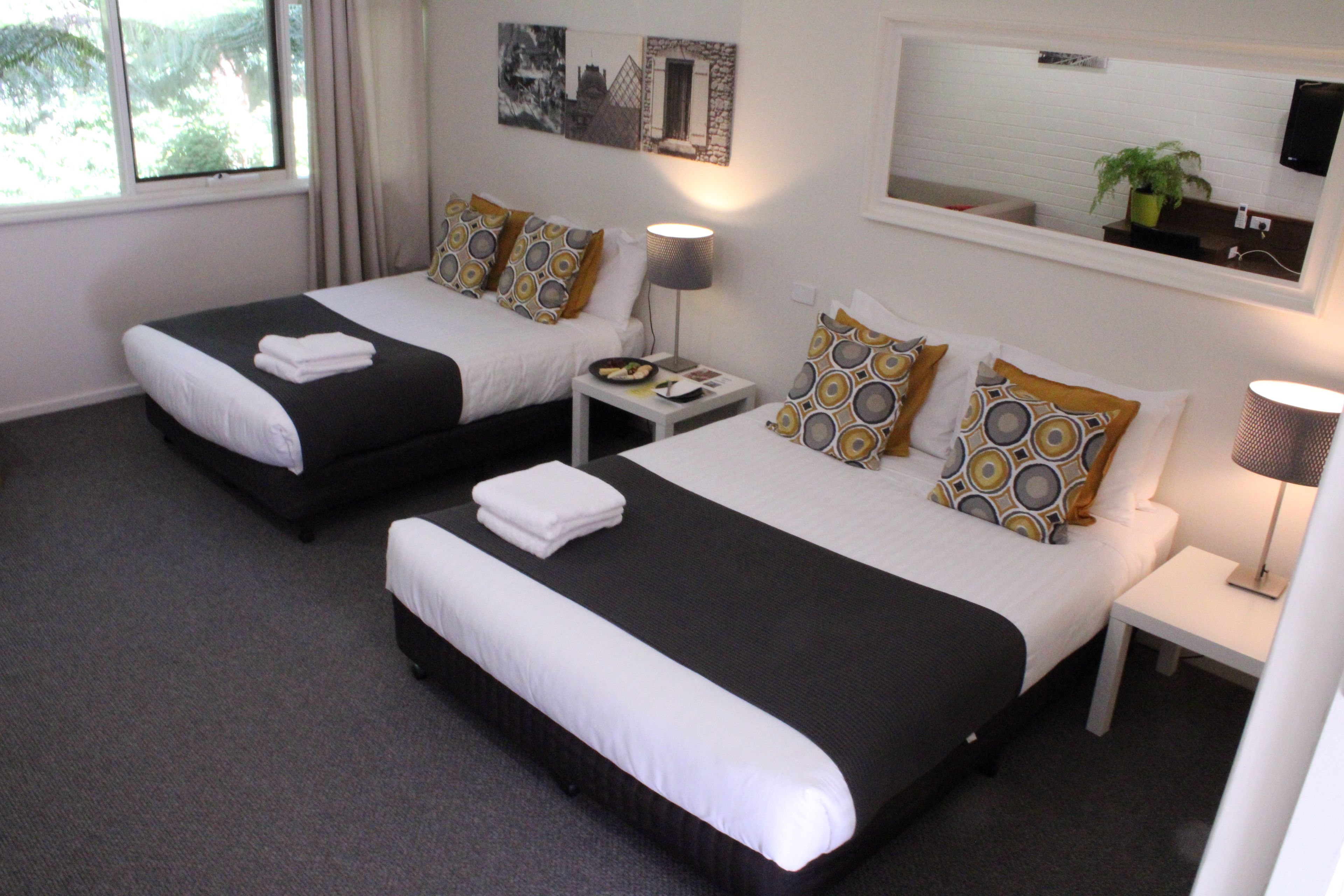 Ein Hotelzimmer mit zwei Einzelbetten, jeweils mit einer schwarz-weißen Tagesdecke, einem kleinen Nachttisch mit Lampe und einem an der Wand montierten Fernseher.