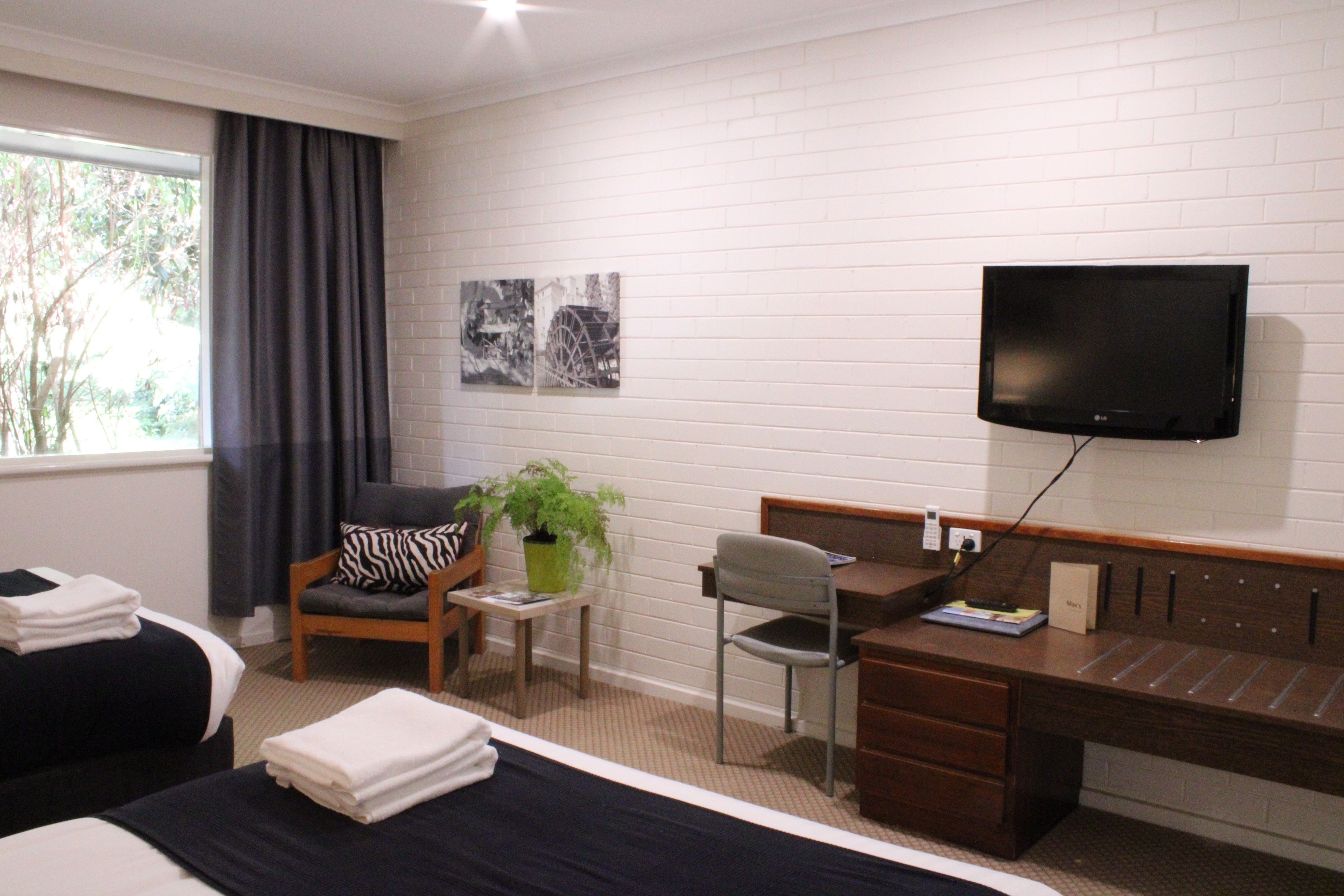 A hotel room with two beds, a desk, a chair, a television, and artwork on the wall.