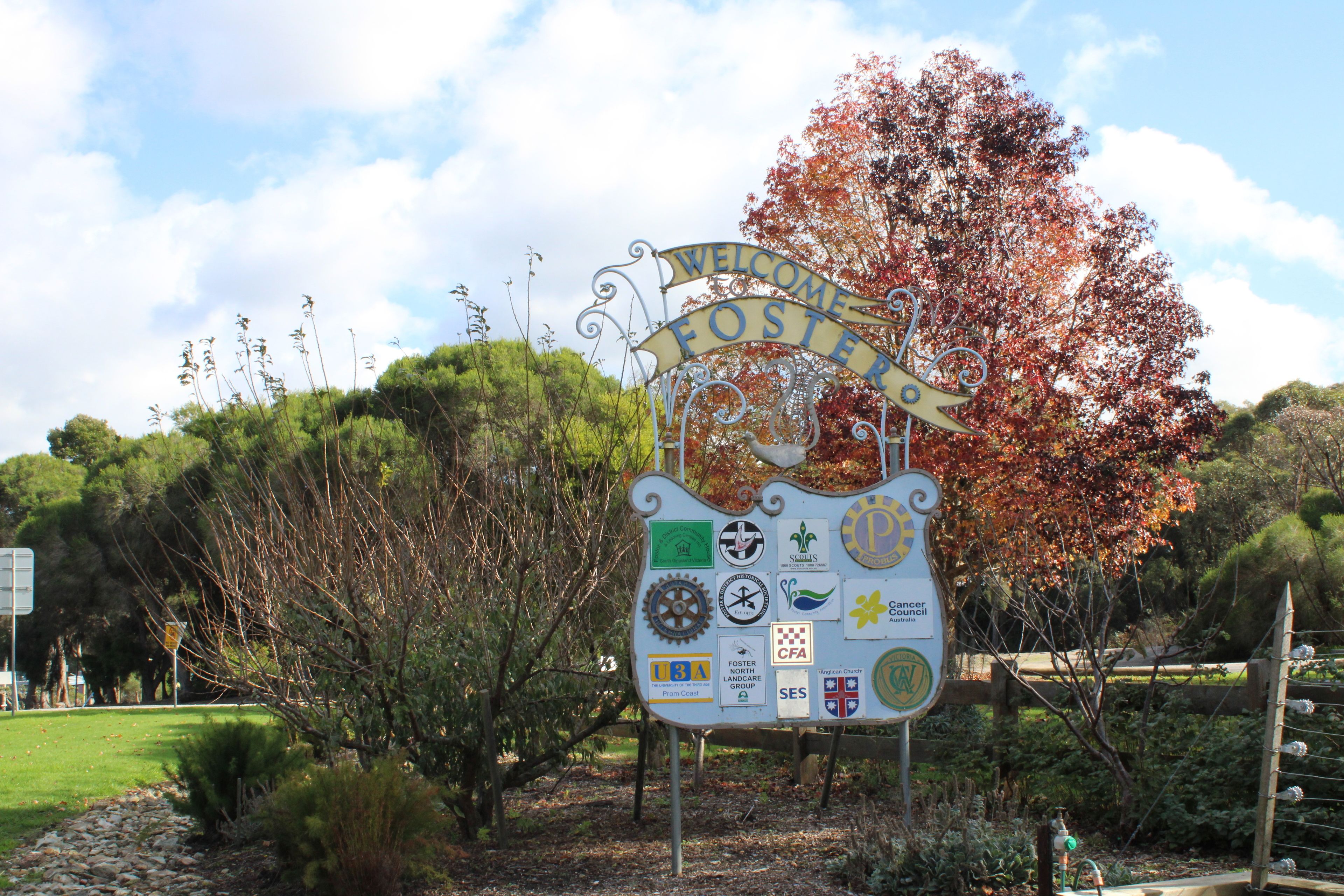 Un letrero de bienvenida con varios logotipos y un jardín.