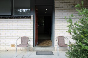 A building entrance with a brick wall, two wicker chairs, a Christmas tree, and a door marked with the number 8.