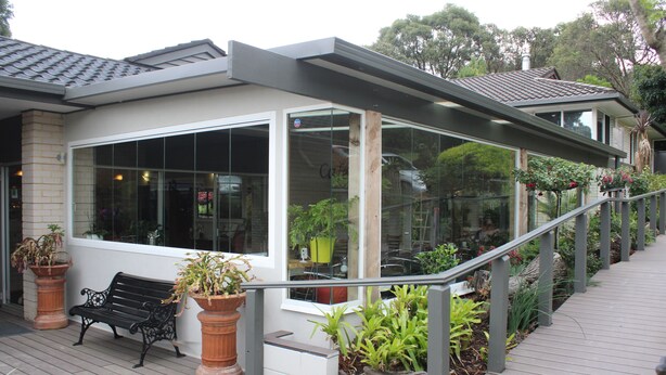A modern building with large windows, a wooden deck, and potted plants. - Prom Country Lodge (Foster)