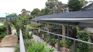 A modern building with a covered walkway, surrounded by lush greenery and a large rock. - Prom Country Lodge (Foster)