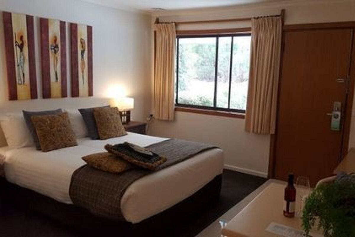 A hotel room with a bed, bedside table, lamp, window with curtains, and a TV.