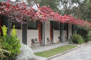 A building with a brick facade, multiple windows, and a covered outdoor seating area with chairs.