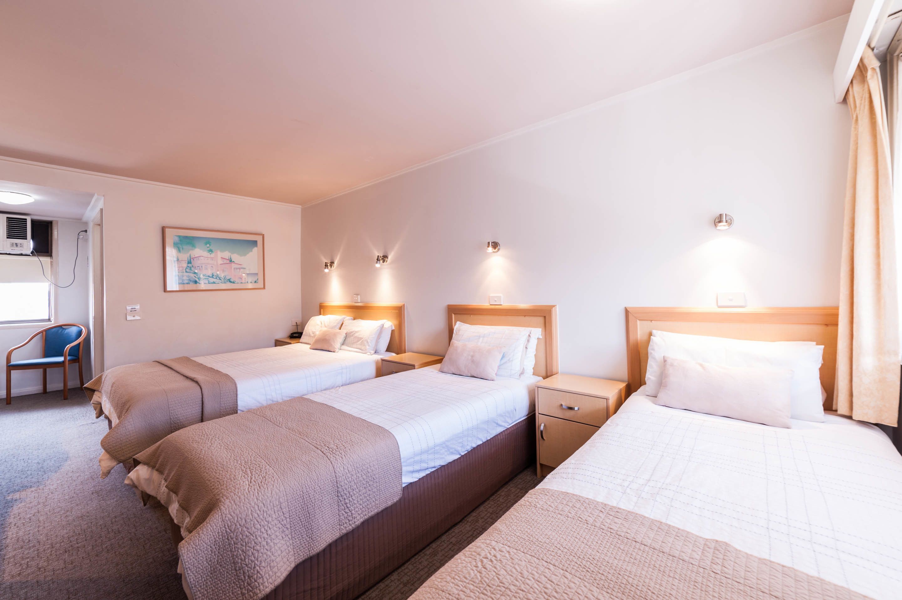 A hotel room with three beds, a desk, and a chair.