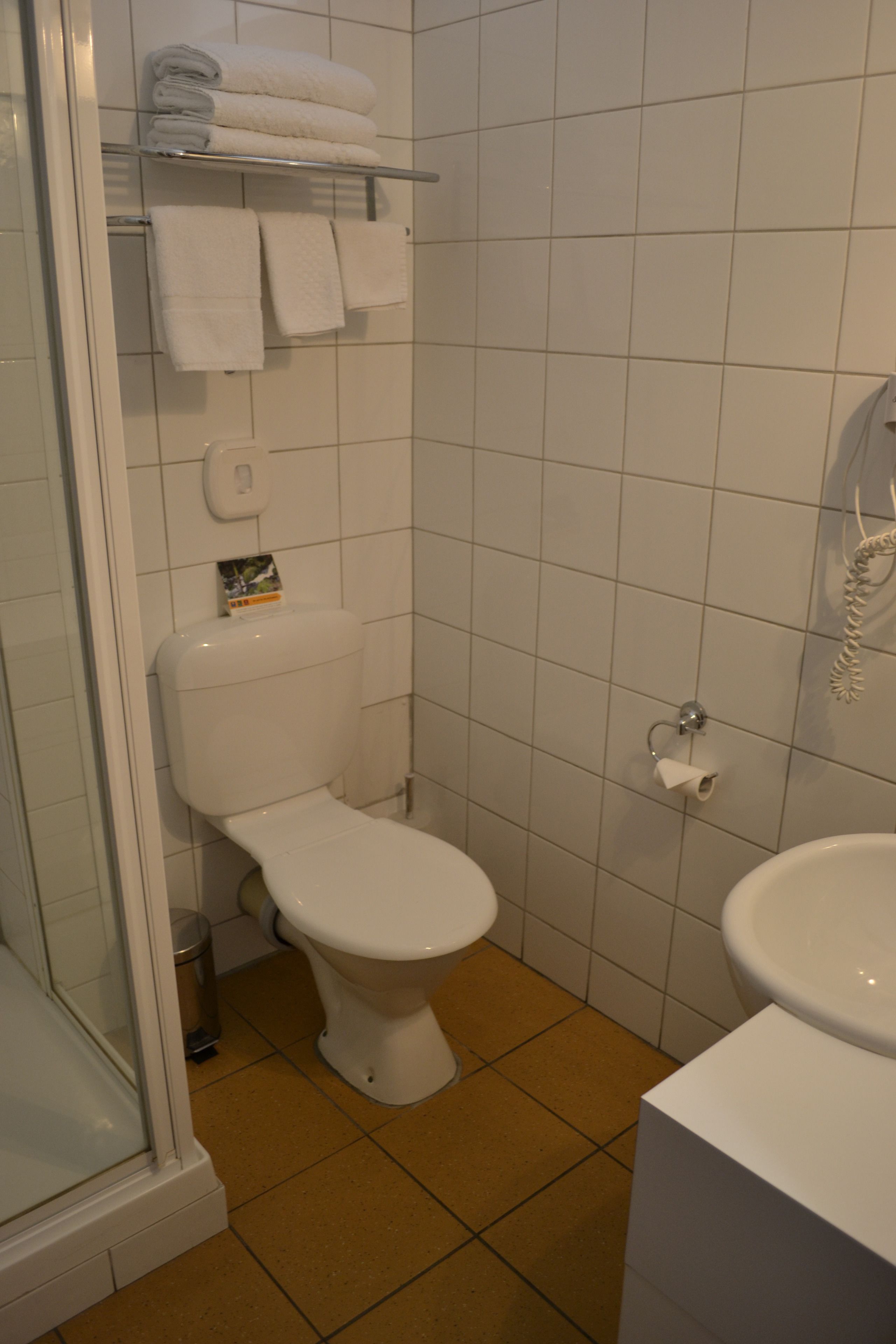 Un baño con inodoro, lavamanos, ducha y estante con toallas.