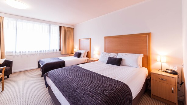 A hotel room with two beds, a desk, and a chair.