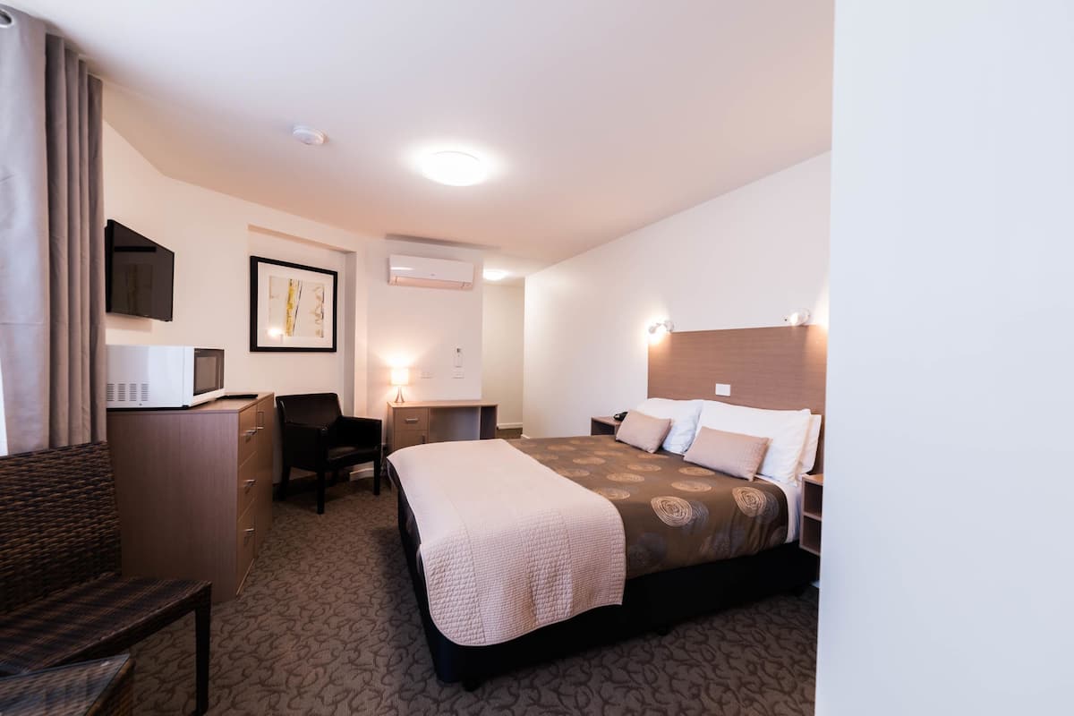 A hotel room with a bed, desk, chair, and a television.