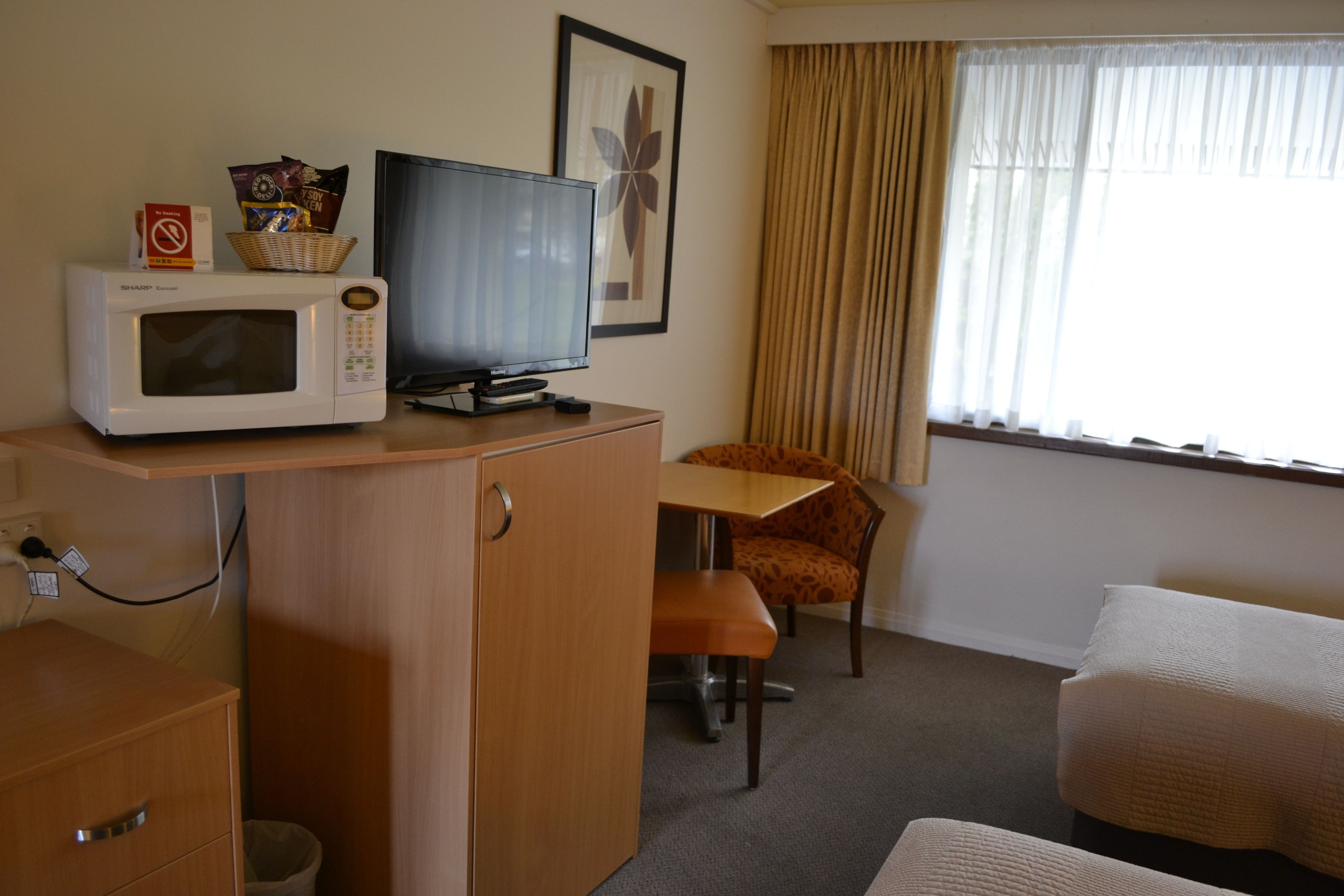 A hotel room with a wooden desk, a television, a microwave, a chair, and a bed.