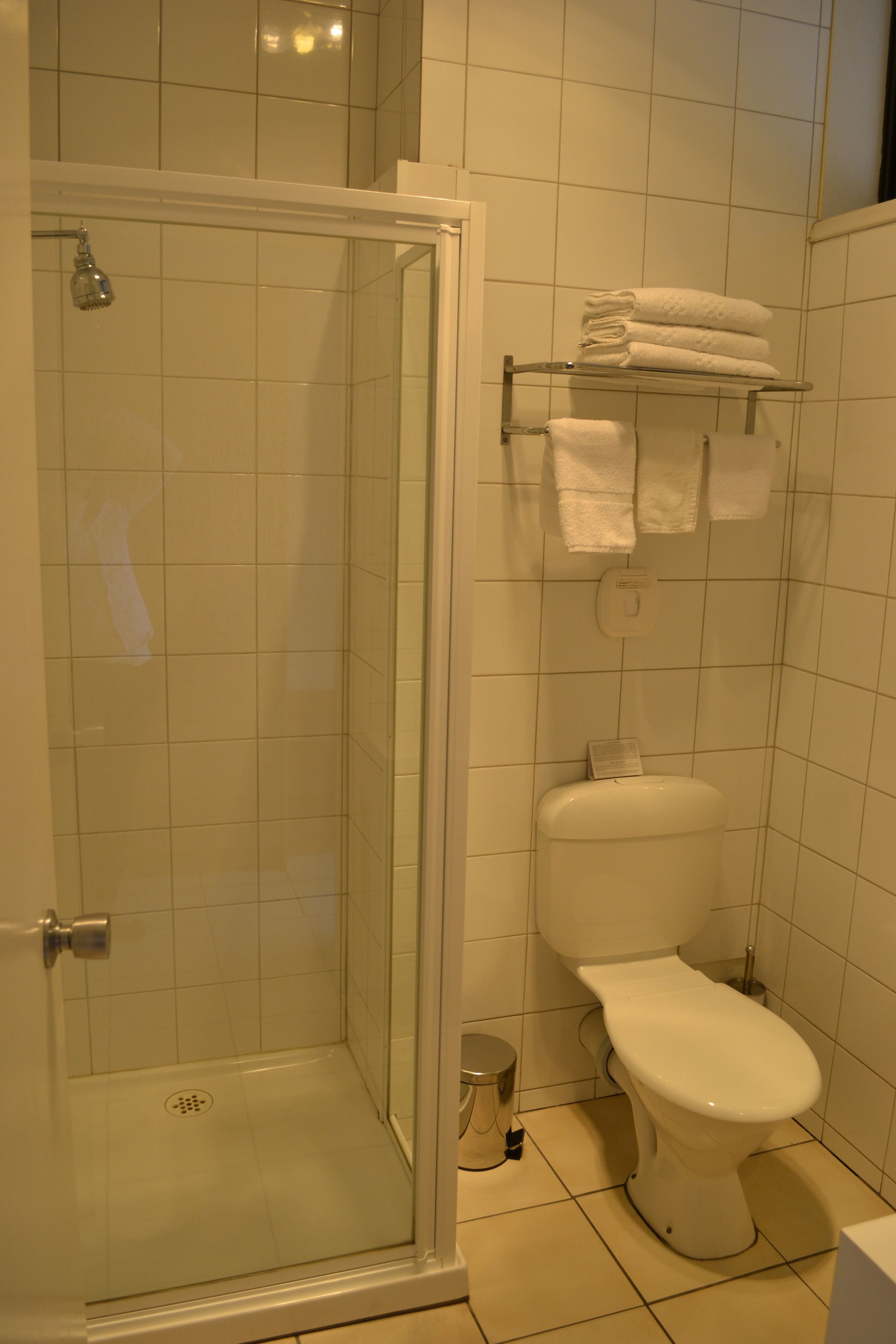 A bathroom with a glass shower enclosure, a toilet, and a towel rack with folded towels.