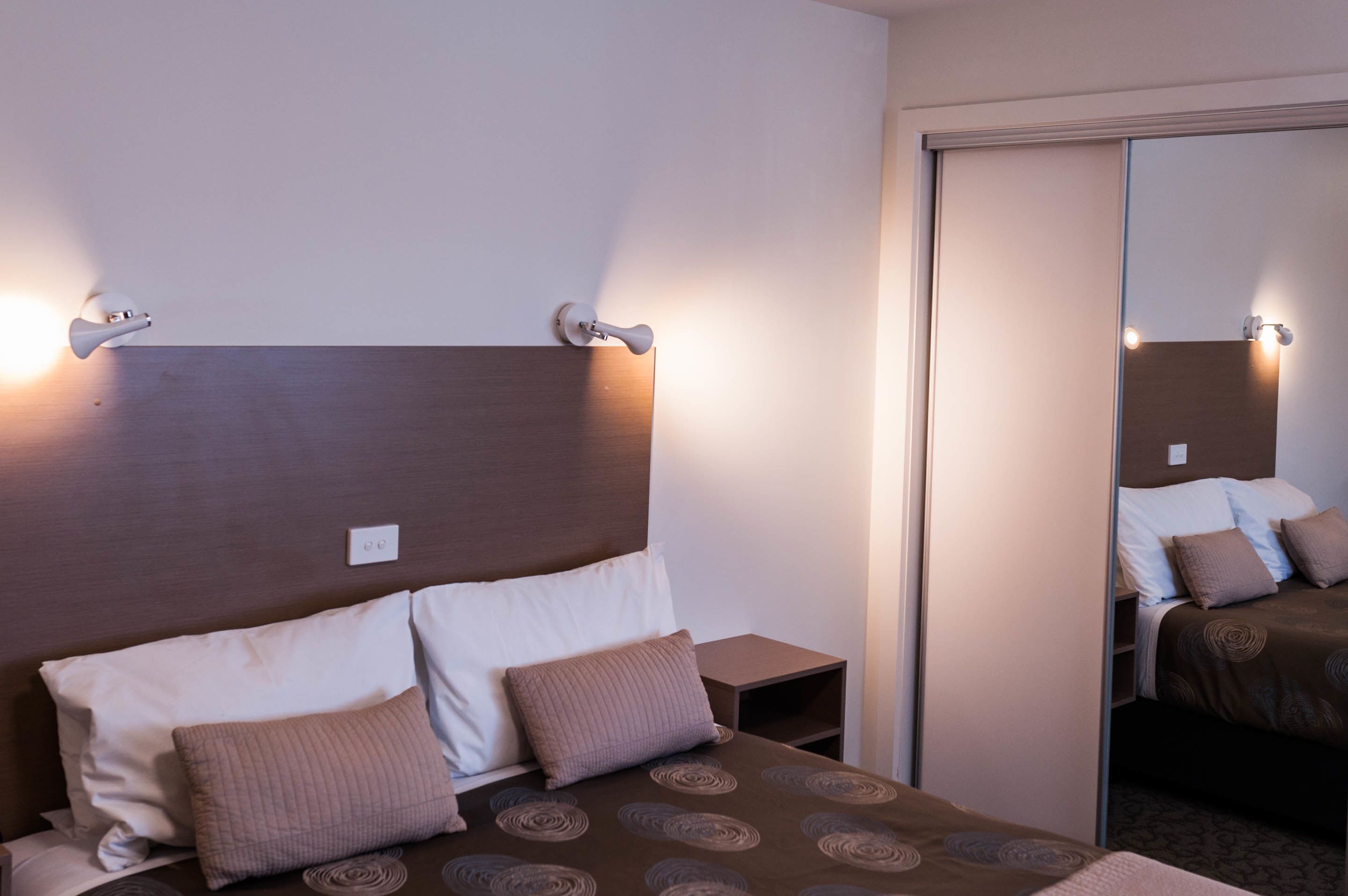 Une chambre d’hôtel avec une tête de lit en bois, deux tables de chevet, un miroir et un lit avec une literie à motifs.