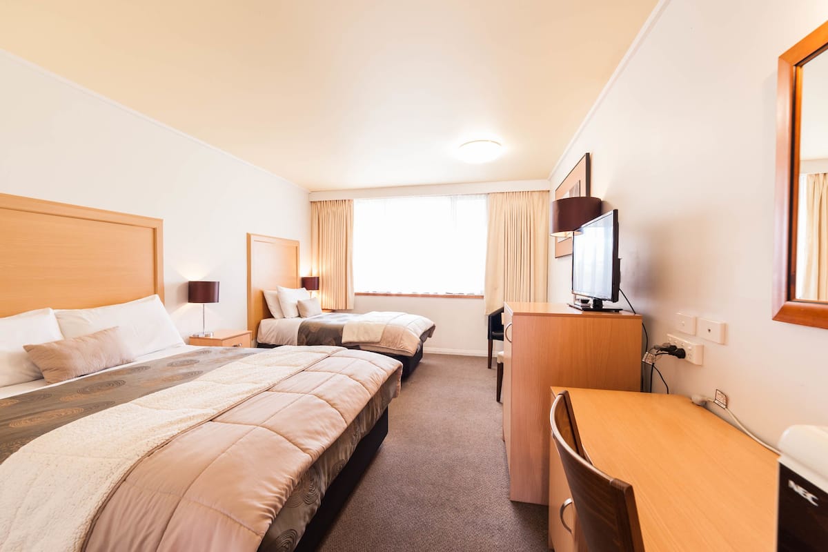 A hotel room with two beds, a desk, a TV, and a window with curtains.