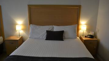 Una cama bien hecha con almohadas blancas y negras, dos lámparas de noche y mesitas de noche de madera.