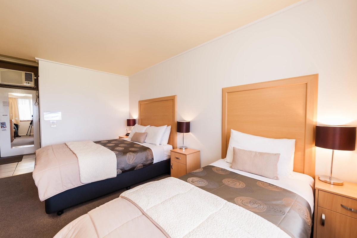 A hotel room with two beds, a wooden headboard, bedside lamps, and a small bedside table.