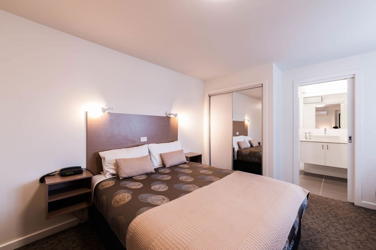 A hotel room with a bed, bedside tables, a mirror, and a bathroom visible through an open door.