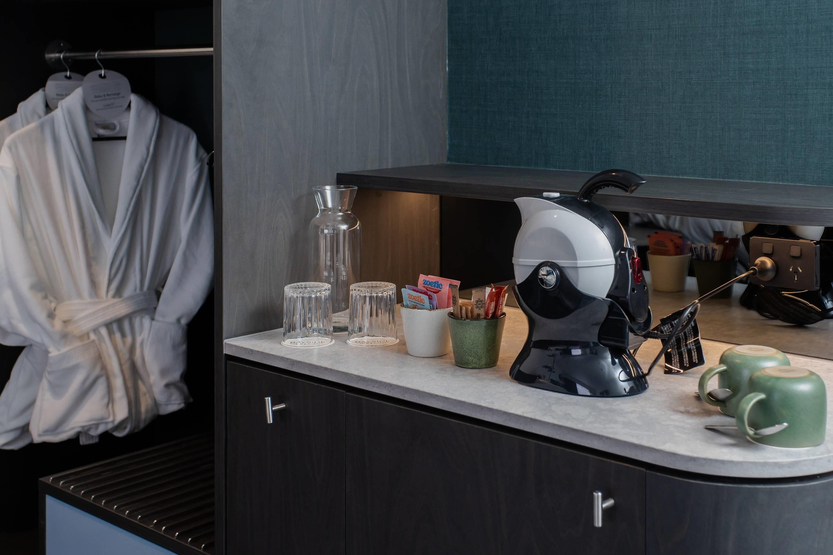 Ein modernes Badezimmer mit Waschtisch, einer Kaffeemaschine, einem Handtuchhalter und einem Spiegel.