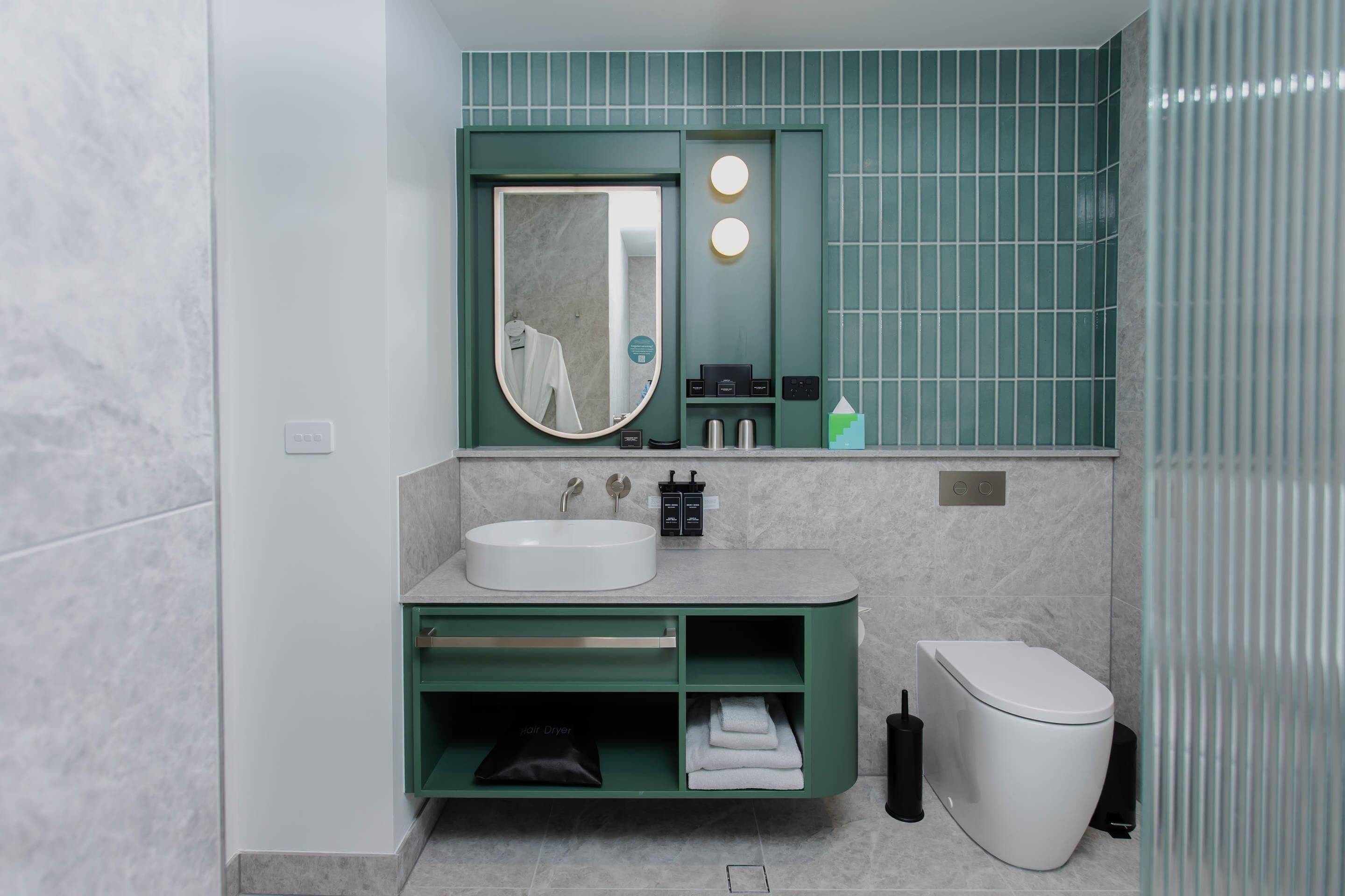 A modern bathroom with a white sink, green vanity, a mirror, and a toilet.