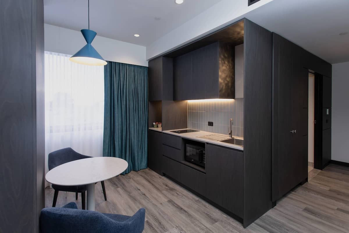 Een moderne keuken met donkere kastjes, een wit aanrecht en een blauwe hanglamp.