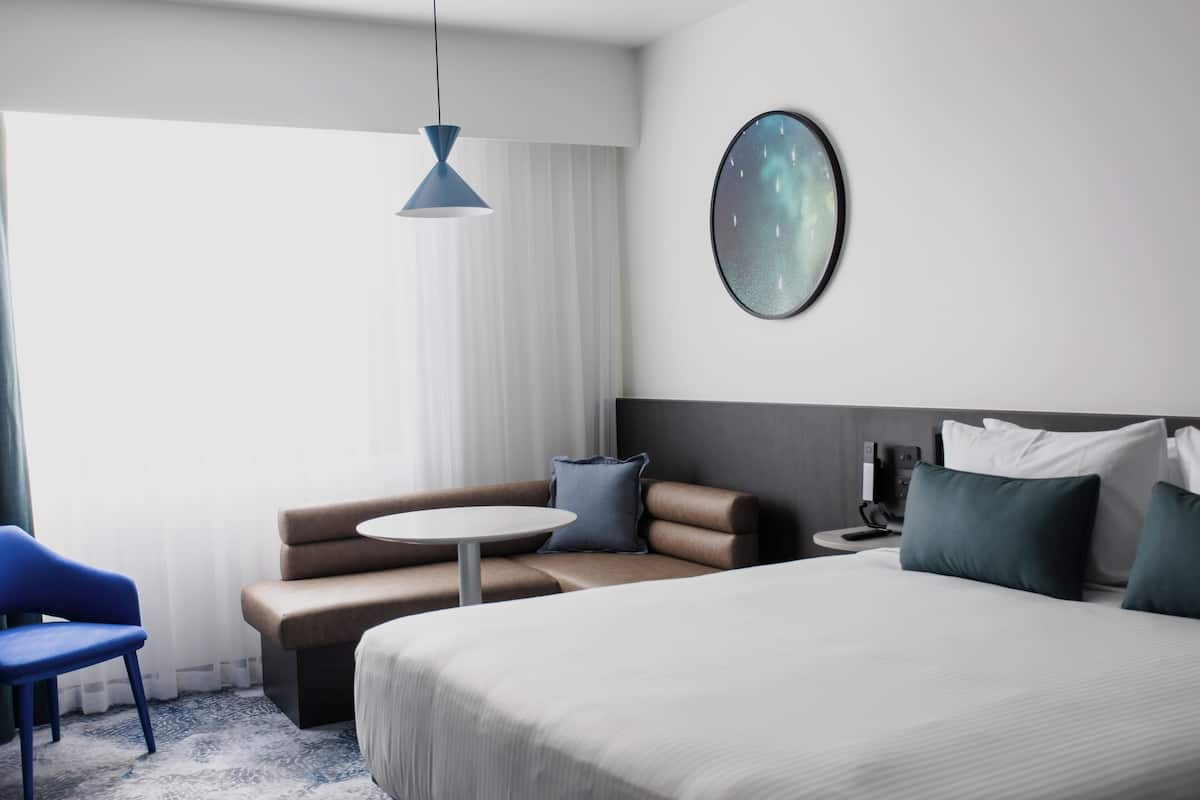 Een moderne hotelkamer met een groot bed, een ronde tafel, een bank en een blauwe stoel.
